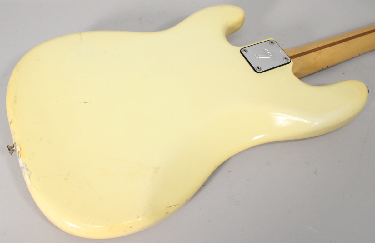 The back of an Olympic White bass guitar body, showing a chrome neck plate, a worn strap button, and many scratches.