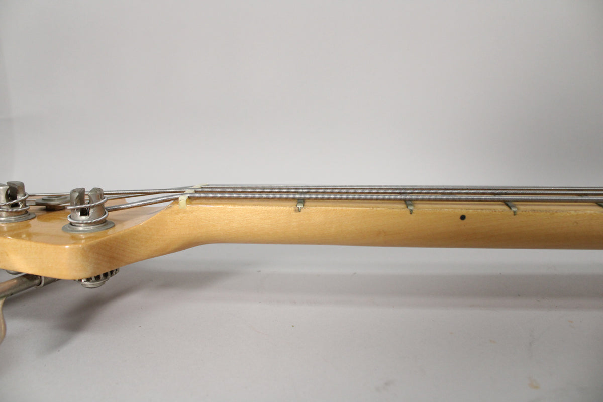 Close-up of the bass neck and headstock from the side, showing the light maple finish, tuning pegs, and string tree.
