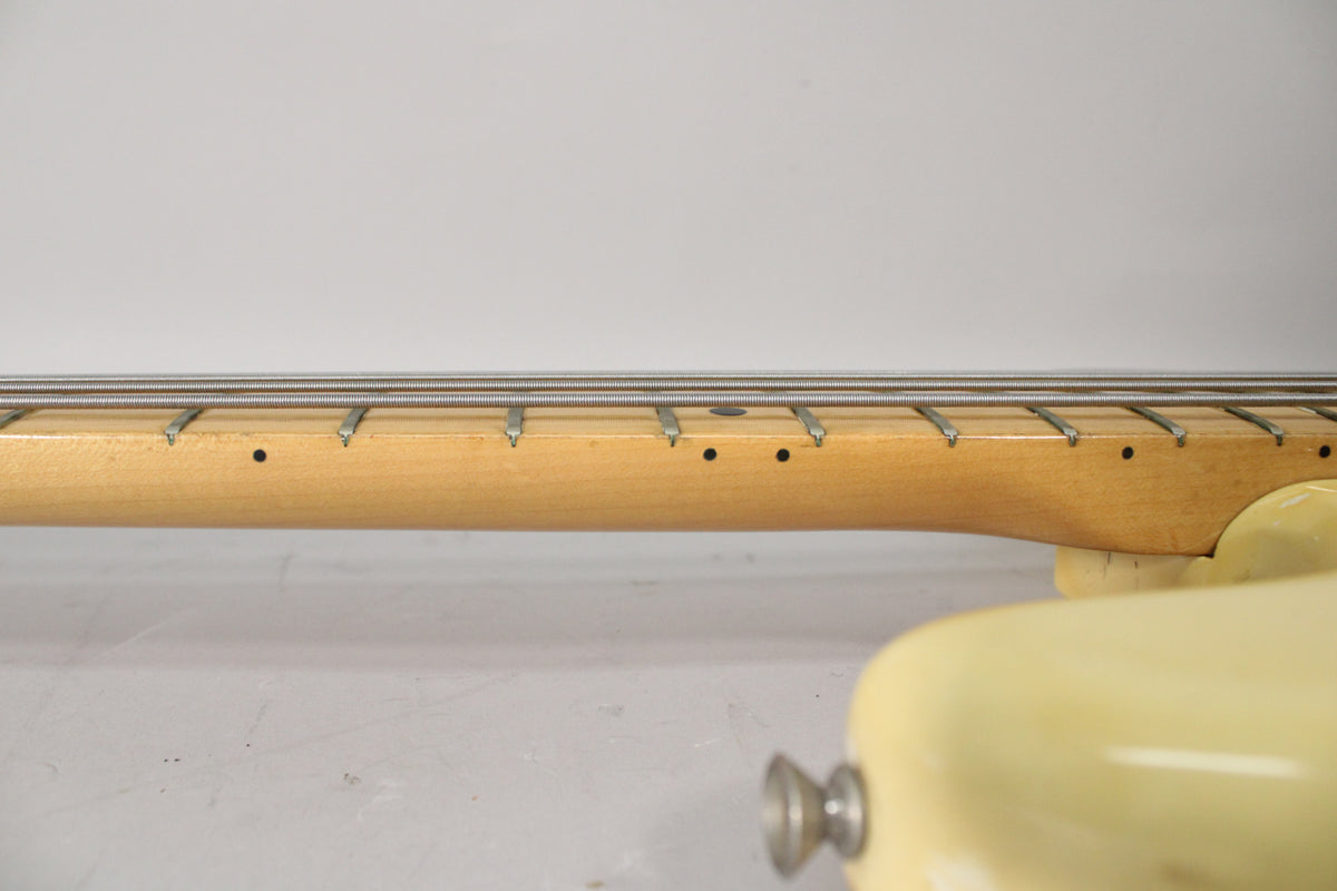 Close-up of the bass neck, showing the light maple fretboard with black dot inlays and four strings, joining the Olympic White body.