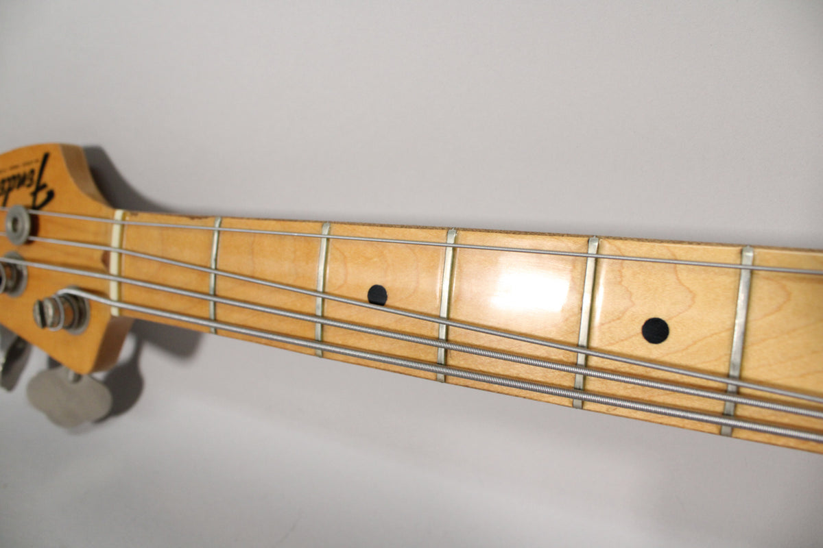Close-up of the bass neck and headstock, showing a maple fretboard with black dot inlays and four silver tuning pegs.