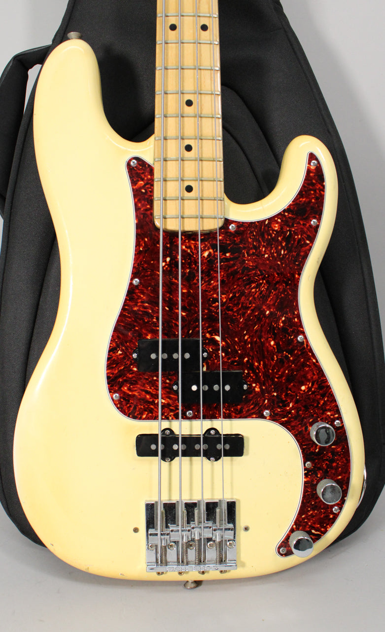 Close-up of the bass's yellowed body, showing a tortoiseshell pickguard, two black pickups, chrome bridge, and three control knobs.