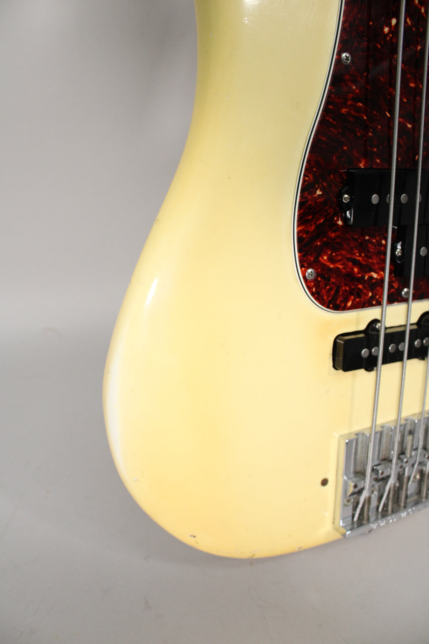 Close-up of the bass body's lower bout, showing the aged Olympic White finish, tortoiseshell pickguard, and chrome bridge.
