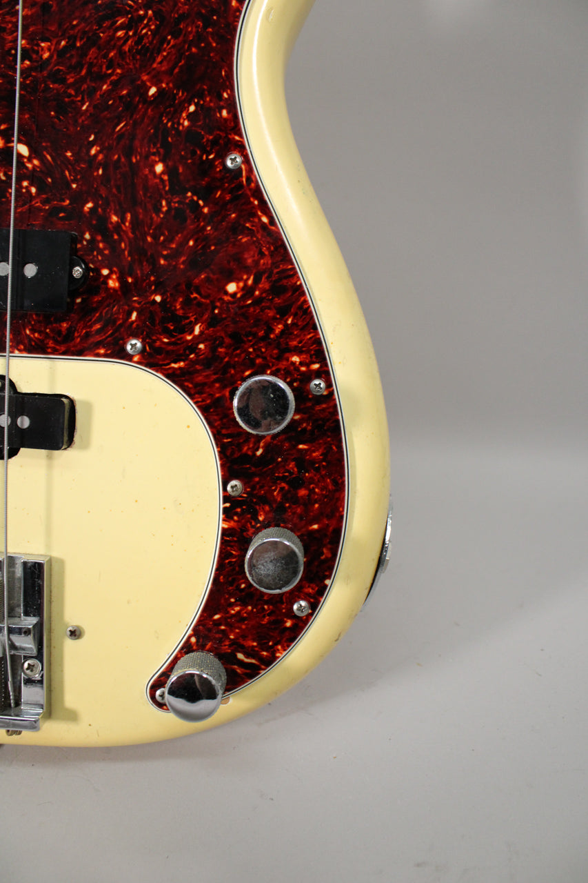 Close-up of a vintage Olympic White Fender Precision Bass body with a tortoiseshell pickguard, showing the bridge, pickup, and control knobs.