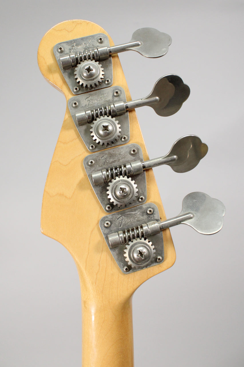 The bass headstock, angled from above, shows four worn, brushed-chrome tuners on a light maple neck.