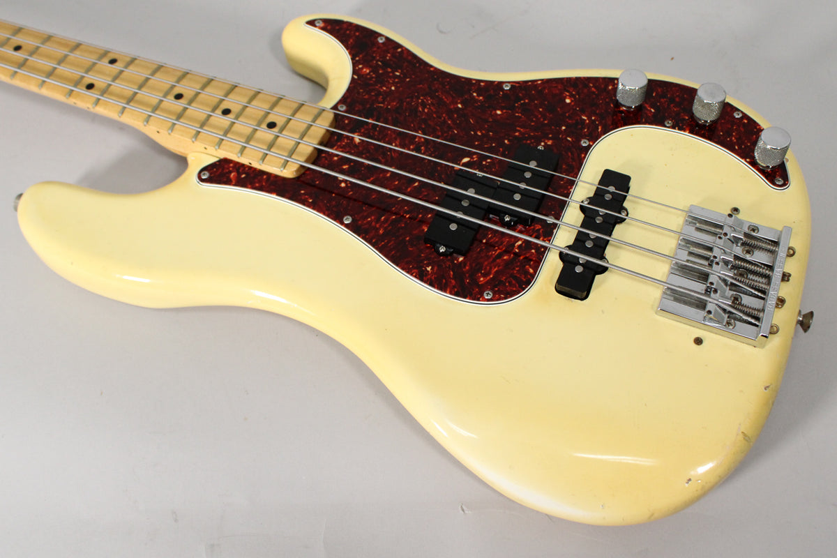 The Olympic White bass body, with a tortoiseshell pickguard, shows visible wear and chips on its lower edge.
