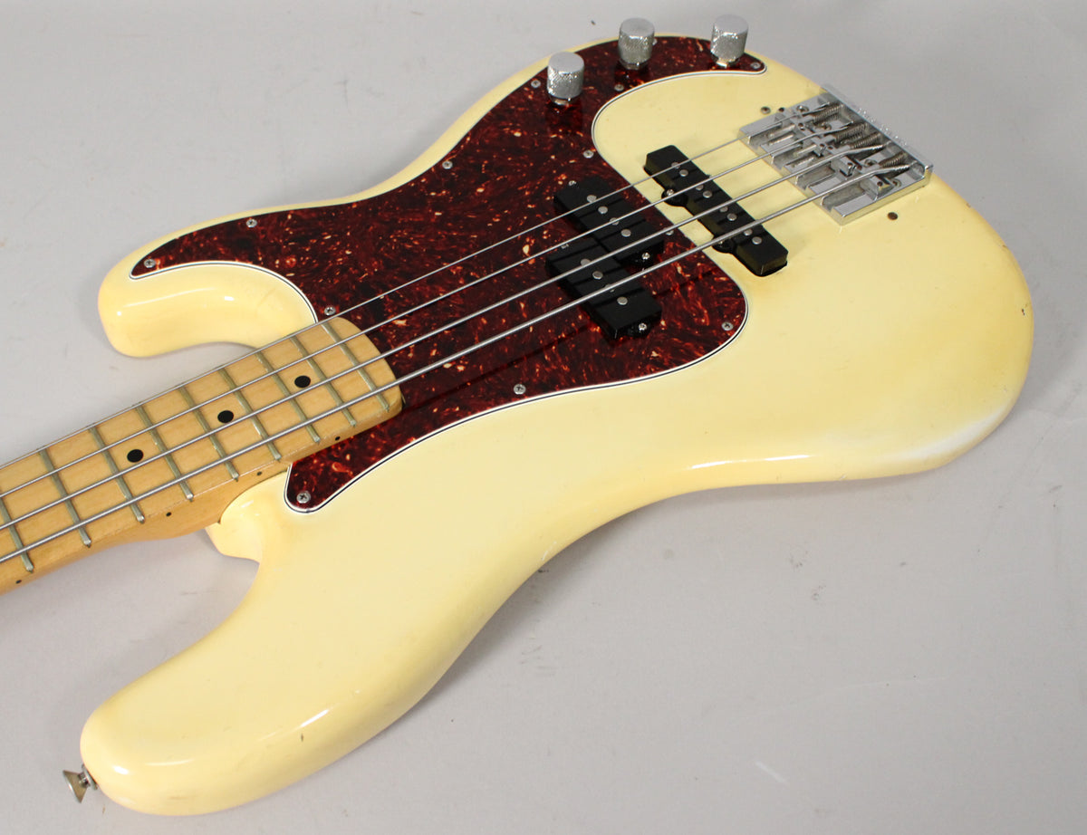 Overhead view of an Olympic White bass guitar with a tortoiseshell pickguard, maple neck, and visible wear on the body edges.