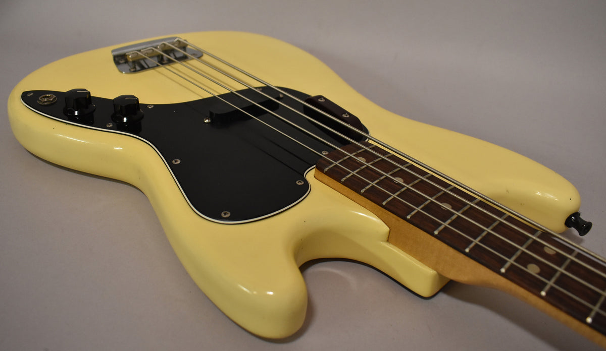 The bass body, in aged Olympic White, shows a black pickguard, two control knobs, and a single pickup.