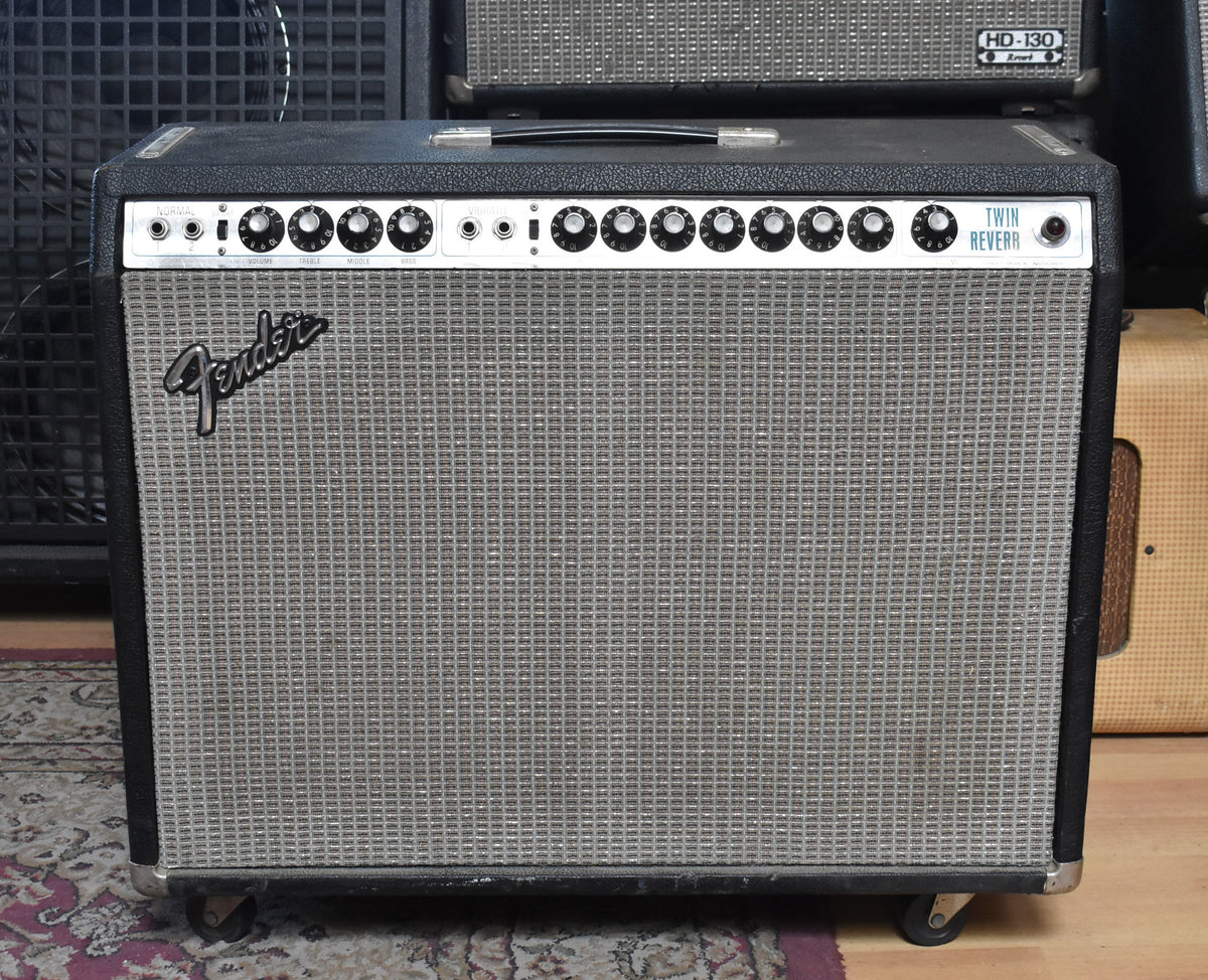 Front view of a black tolex amp with a silver grille, 12 black control knobs, and four casters.