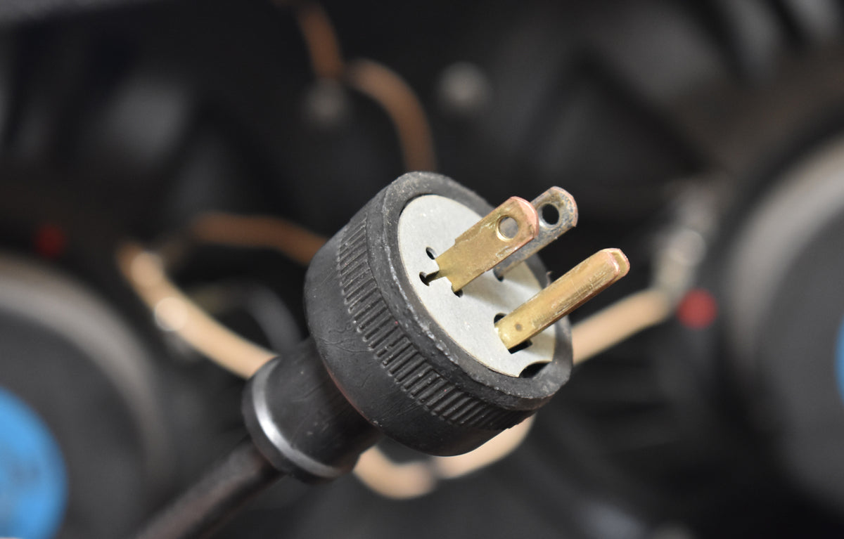 Close-up of the amplifier's black power plug, showing two tarnished brass blades and a round, ribbed rubber housing.