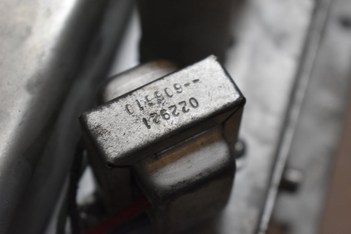 Close-up of a silver metal transformer with stamped numbers "022921" and "015509--605510", showing some wear and dust.