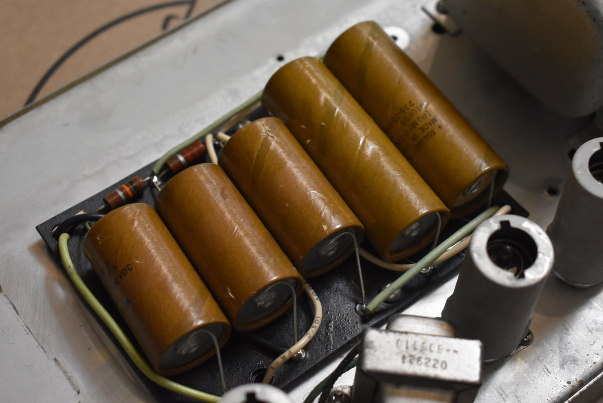 A close-up of the amplifier's internal components, showing five large, tan cylindrical capacitors and various wires on a black board.