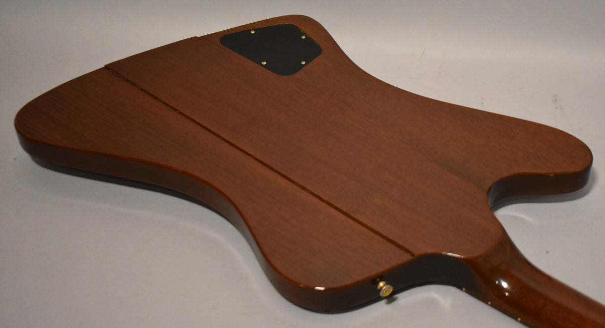 The guitar's reverse body, with a dark brown satin finish, is viewed from the back, showing a black control plate and a glossy neck.