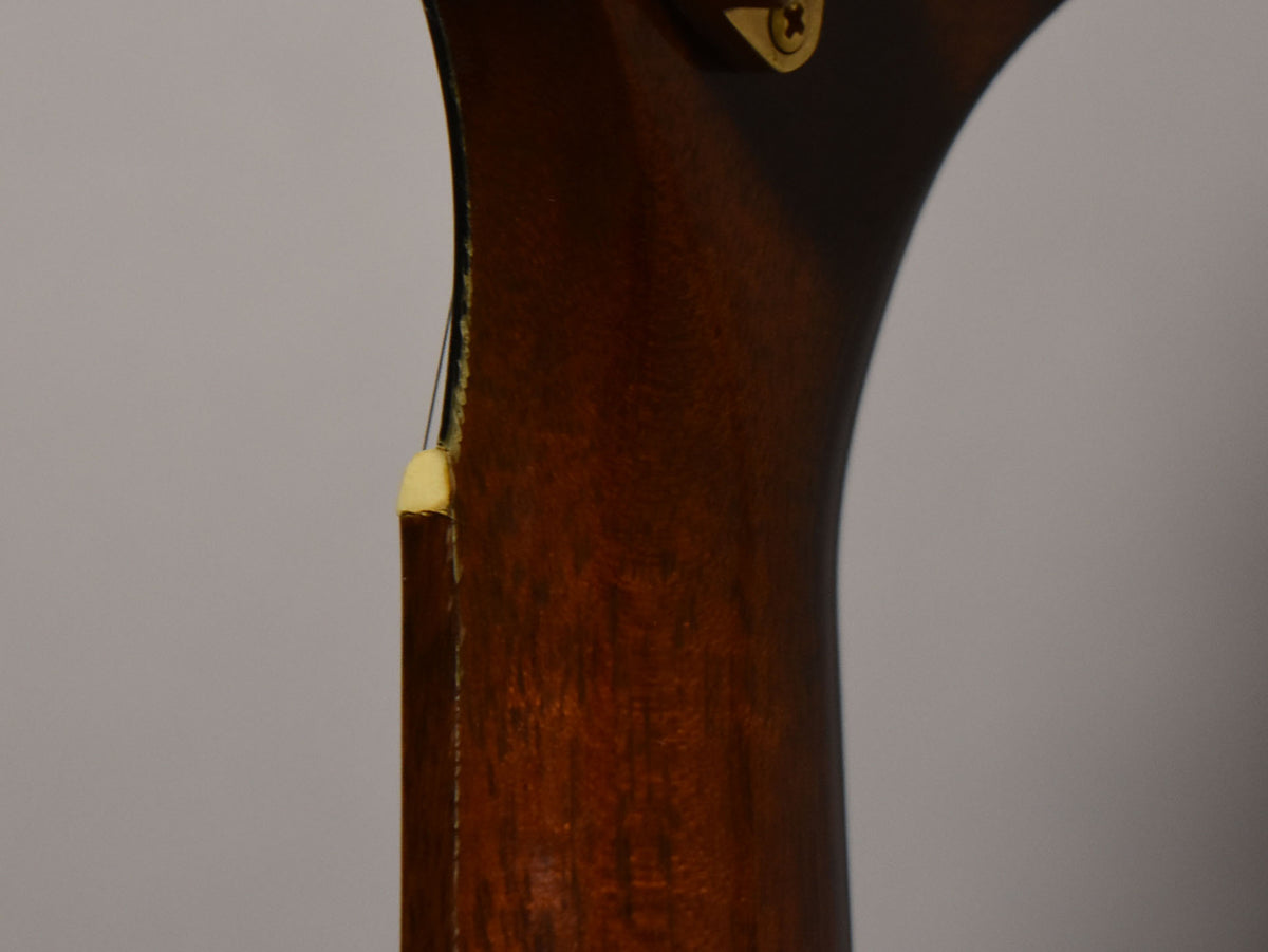 Close-up of the guitar's dark brown neck heel, showing a small chip in the binding and a brass screw head at the top right.