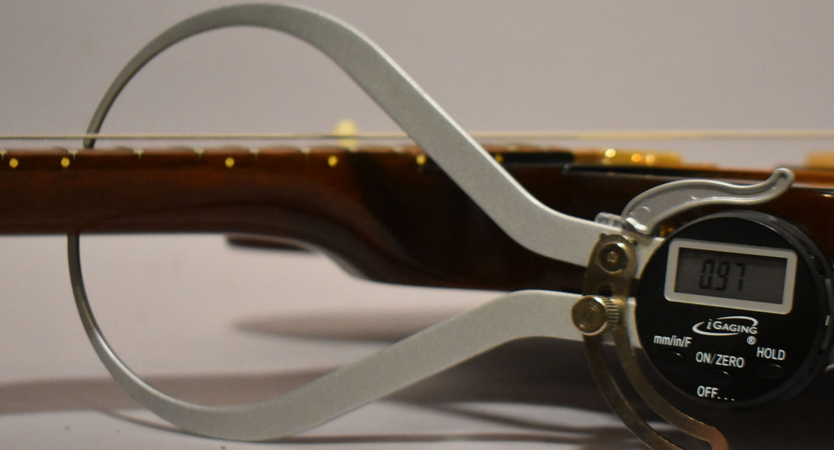A digital caliper measures the string height above the dark brown fretboard with yellow dot inlays.