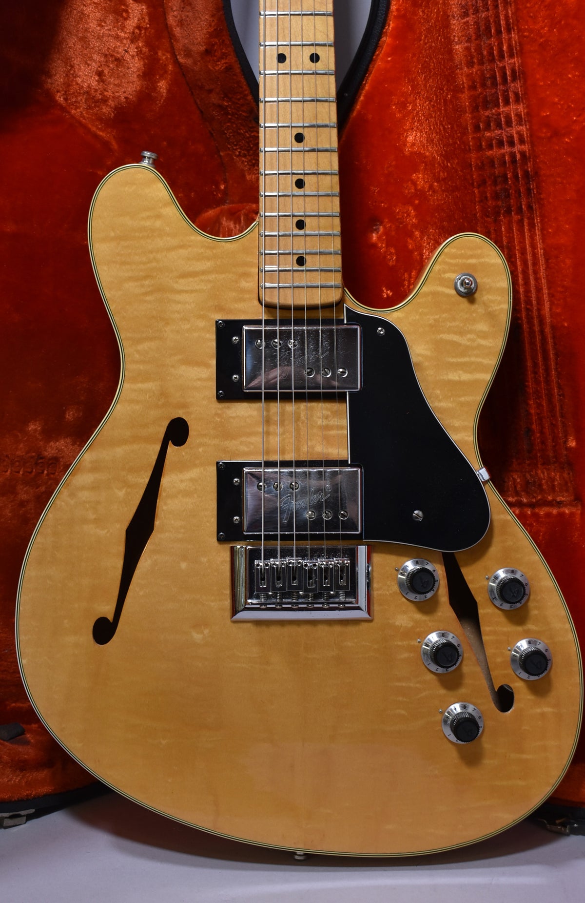 Full-frame view of a natural flame maple semi-hollowbody guitar with two humbuckers, a black pickguard, and four control knobs.