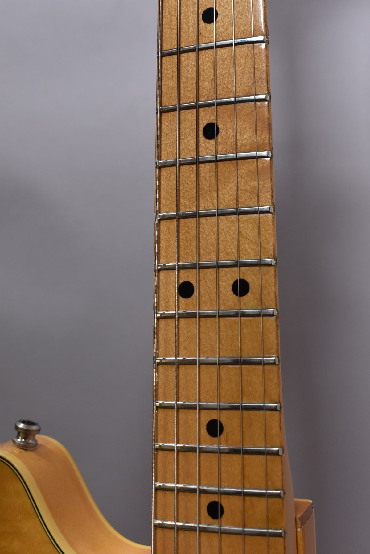 Close-up of the maple fretboard with black dot inlays, showing light wear and a natural flame finish on the neck.