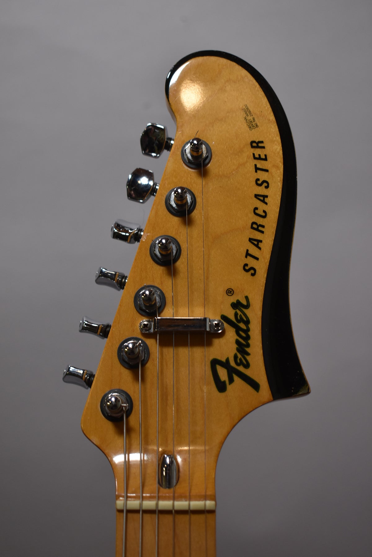 Close-up of the natural flame headstock with black trim, showing six chrome tuners, string tree, and light wear on the edges.