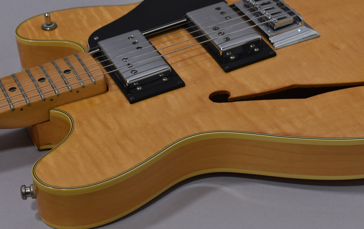 Close-up of the natural flame maple body, showing the neck joint, black pickguard, two chrome humbuckers, and f-hole.
