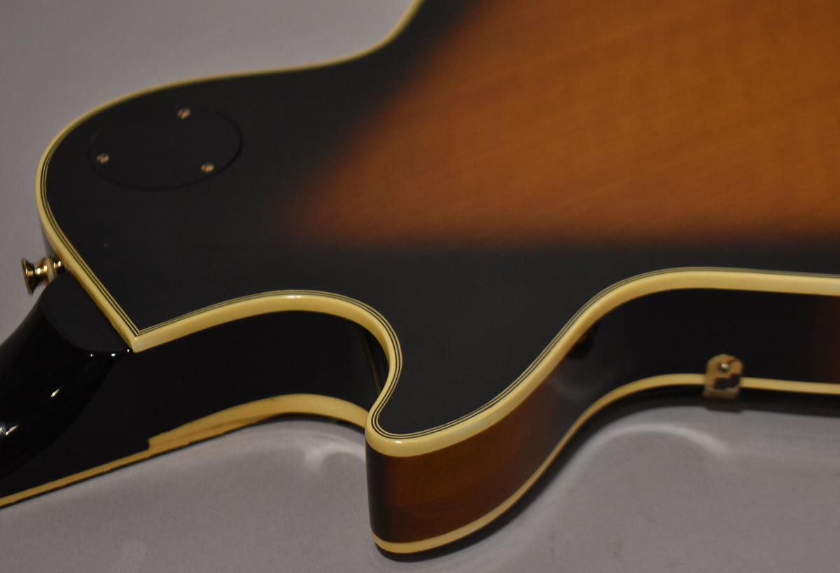 The guitar's tobacco sunburst body, with cream binding and black pinstripes, is shown from the back, angled to reveal the neck heel.
