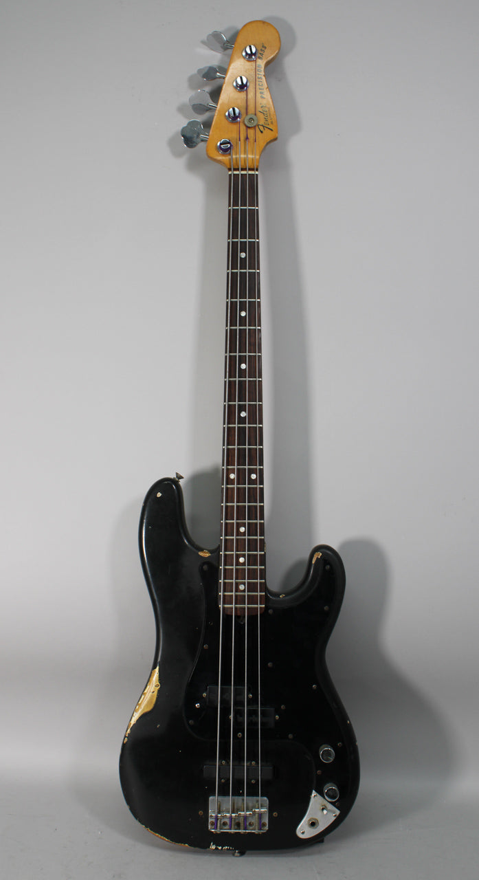 Full-length view of a black bass with a worn finish, revealing gold undercoat, a dark fretboard, and two black pickups.