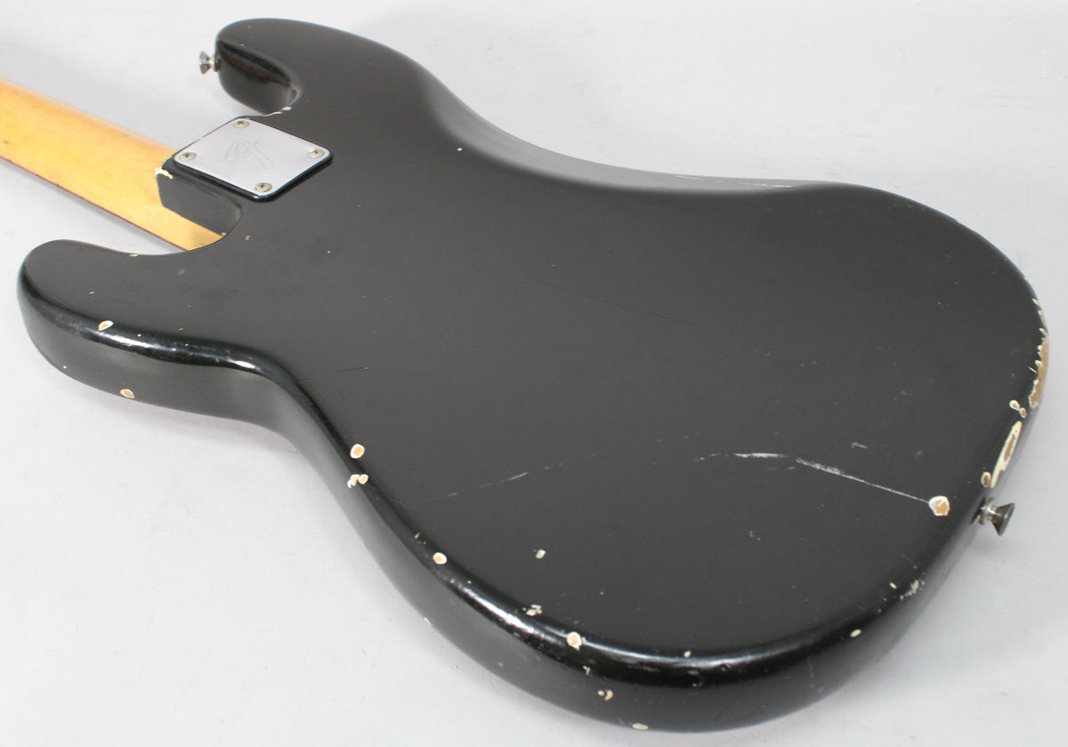 The back of a black bass guitar body, showing heavy wear, chips, and scratches, with a light-colored neck joint.