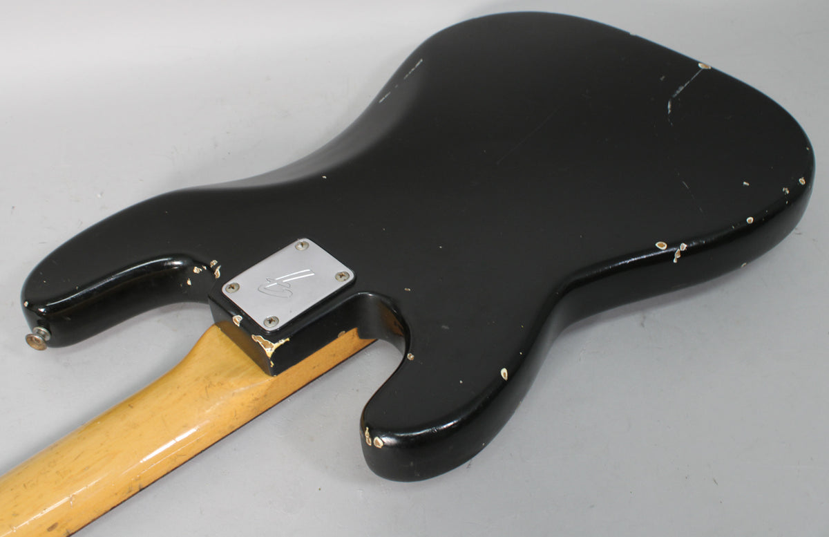 The back of a black bass body, showing a chrome neck plate, a worn maple neck heel, and extensive finish chips and checking.