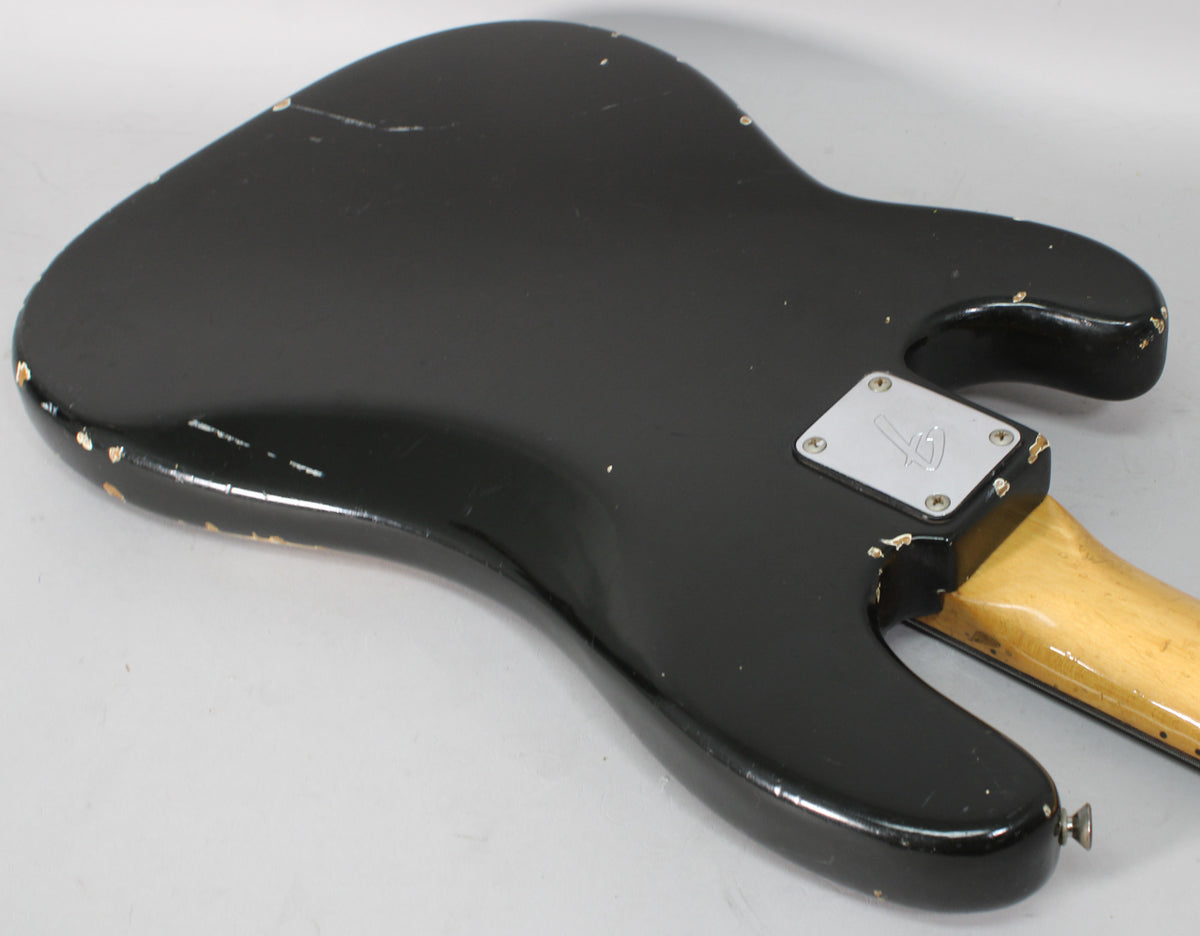 The back of a black bass body, angled from the lower right, shows extensive finish wear, chips, and a chrome neck plate.