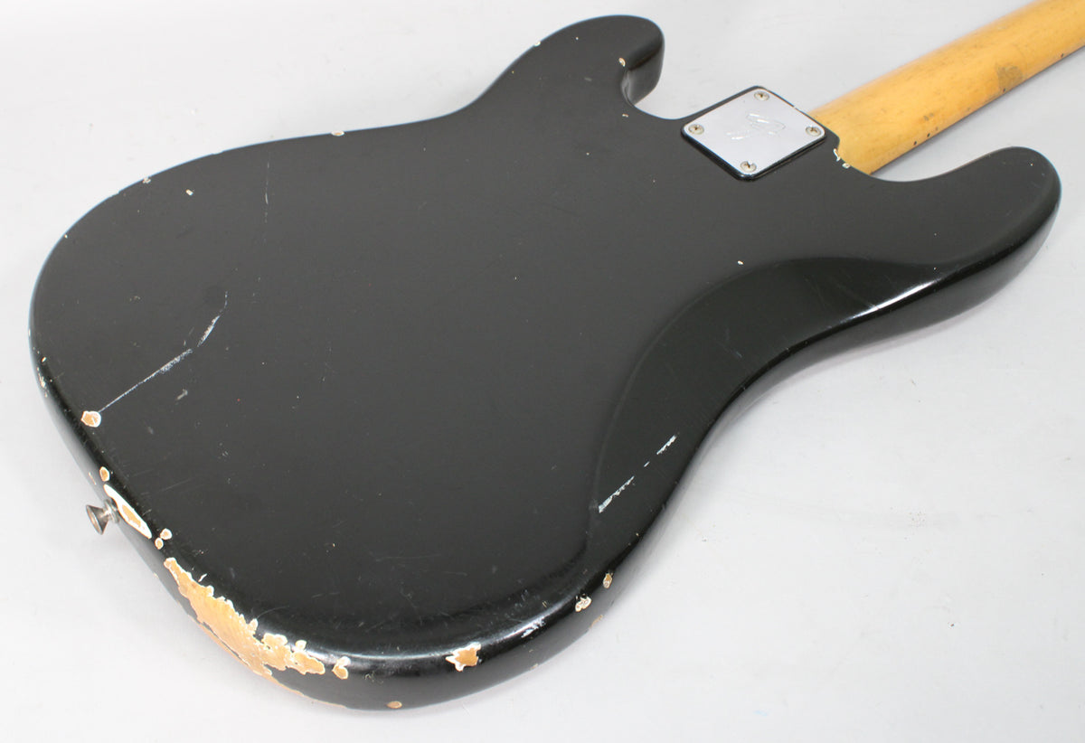 Rear view of a black bass body with heavy finish wear and chipping along the bottom edge, and a chrome neck plate.