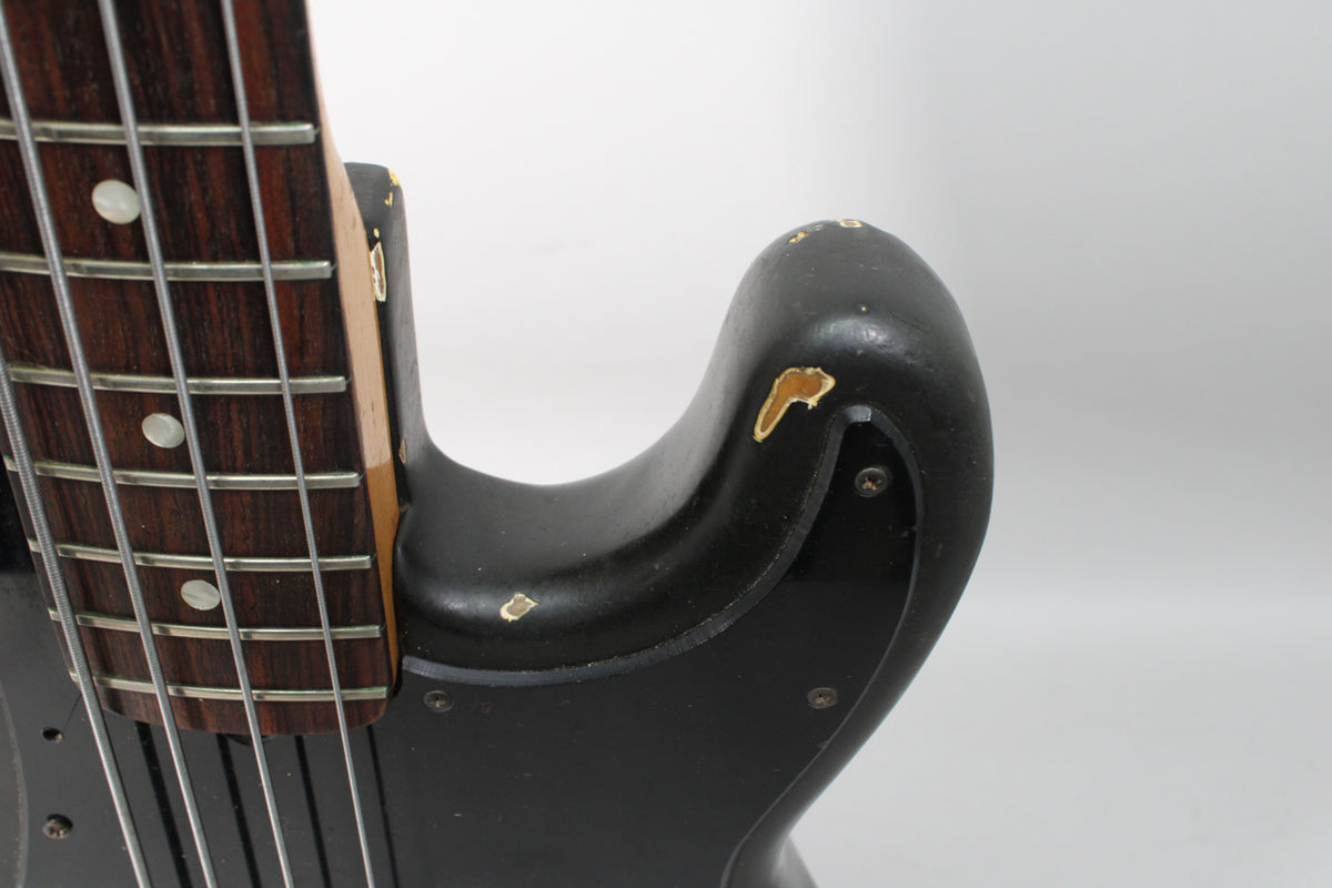 Close-up of the black bass body's upper horn and neck joint, showing significant paint chips and a dark rosewood fretboard.
