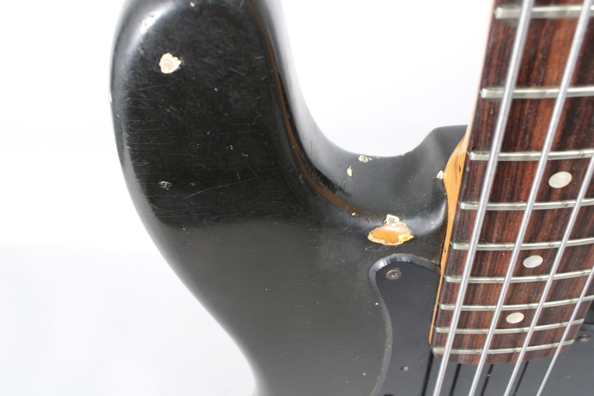 Close-up of the bass's black body near the neck joint, showing significant paint chips revealing the wood beneath.