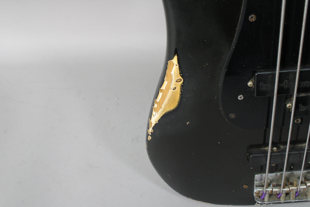 Close-up of the lower bout of a black bass, showing significant paint wear revealing a gold undercoat, and two black Bartolini pickups.