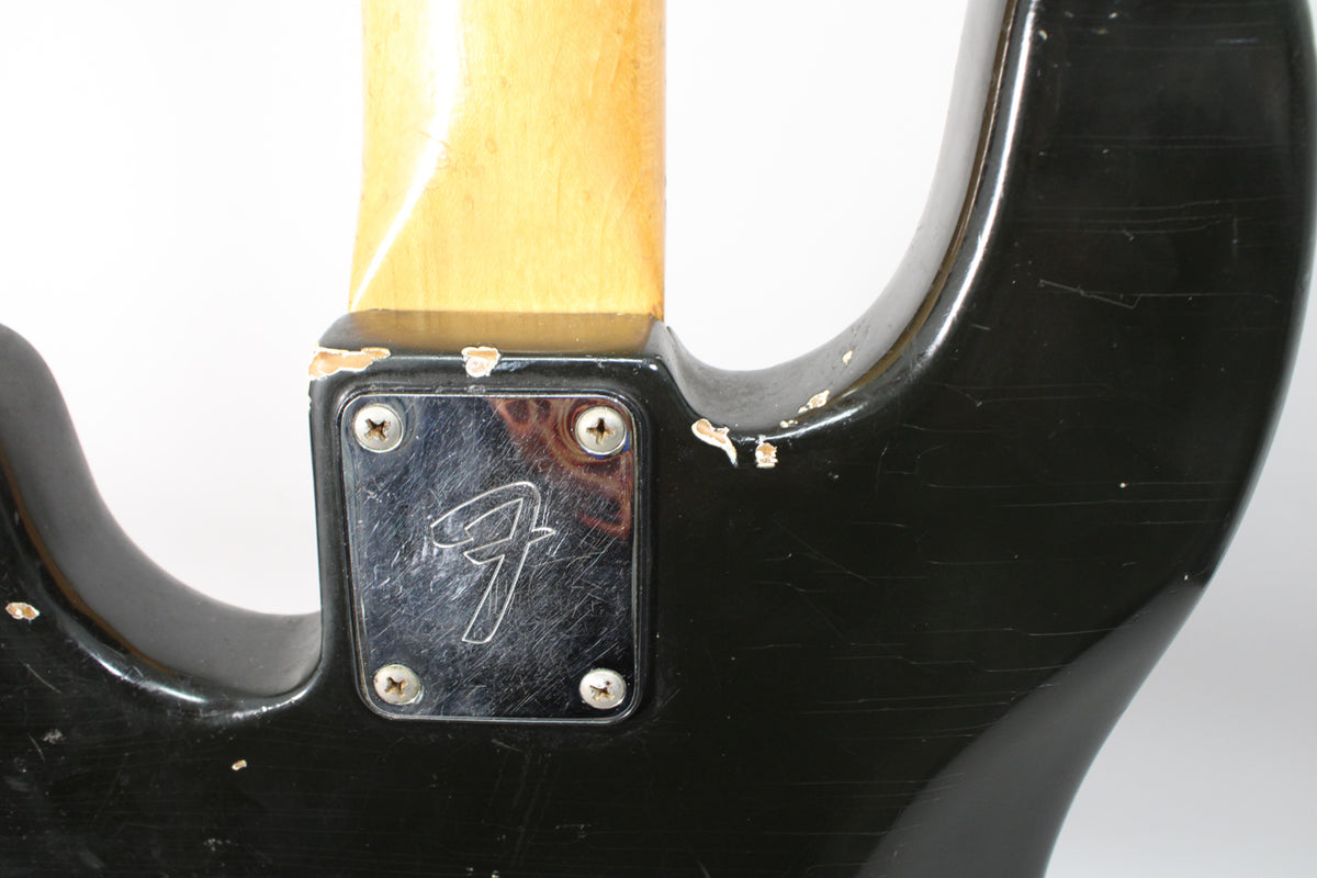 Close-up of the black bass body's neck joint, showing a chrome neck plate with four screws and significant paint chipping and scratches.