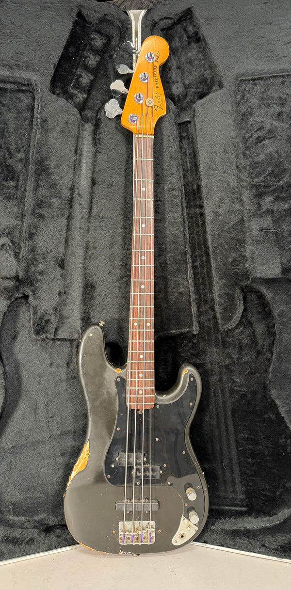 Full-length view of a worn black bass in a black case, showing a P/J pickup configuration and significant paint chipping.
