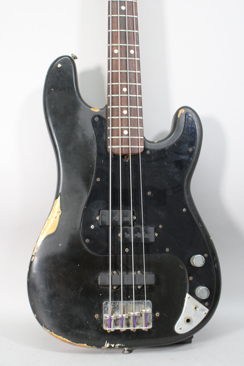 Full front view of a heavily worn black bass with a rosewood fretboard, two Bartolini pickups, and a chrome bridge.