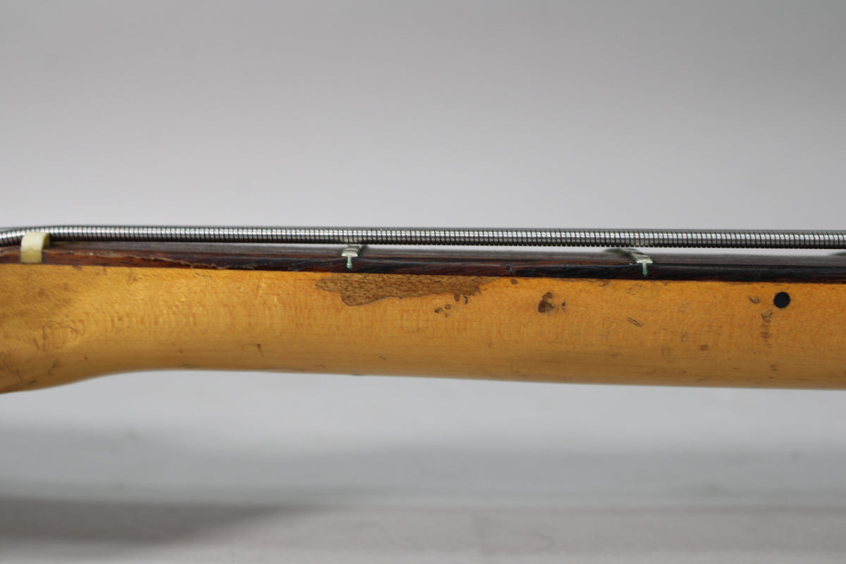 Close-up of the bass neck's side, showing a dark rosewood fretboard, a worn light-brown finish, and four strings.