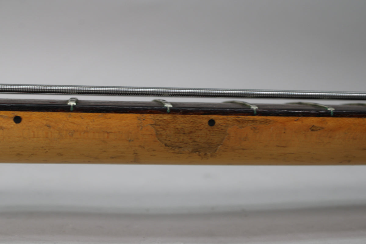 Close-up of the bass neck's worn maple finish, showing dark fretboard, silver strings, and two dark circular fret markers.