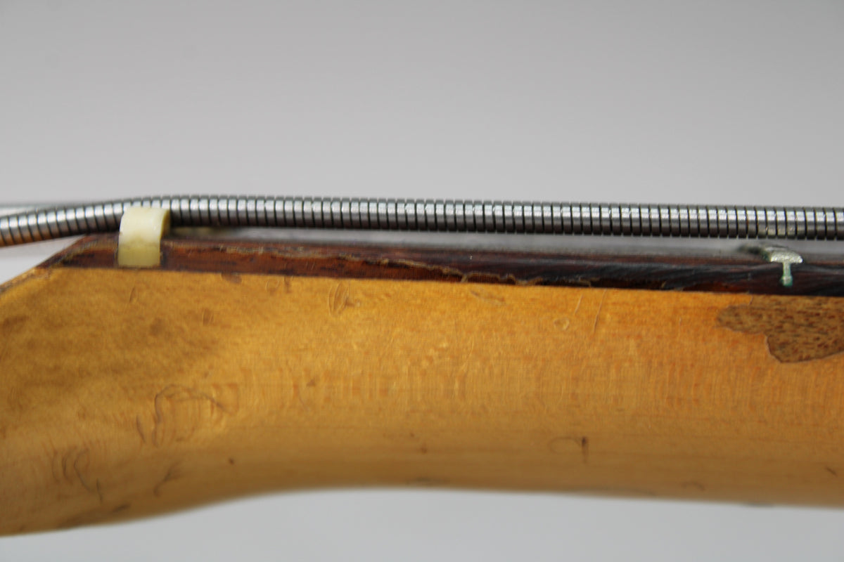 Close-up of the bass neck's side, showing a worn maple finish, dark fretboard, and a cream nut under a bass string.