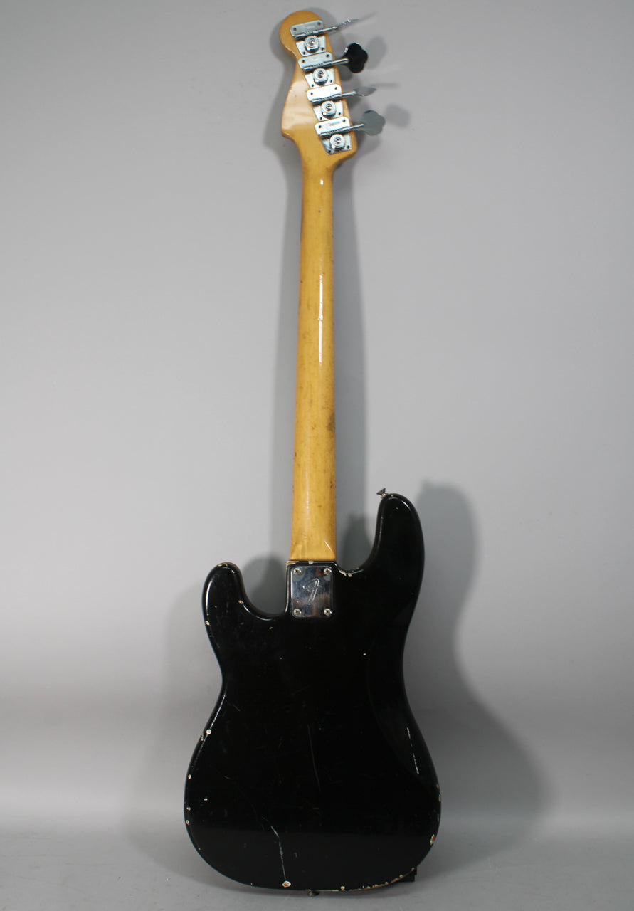 The back of a black bass guitar, showing a worn maple neck, chrome tuners, and heavy finish wear on the body edges.
