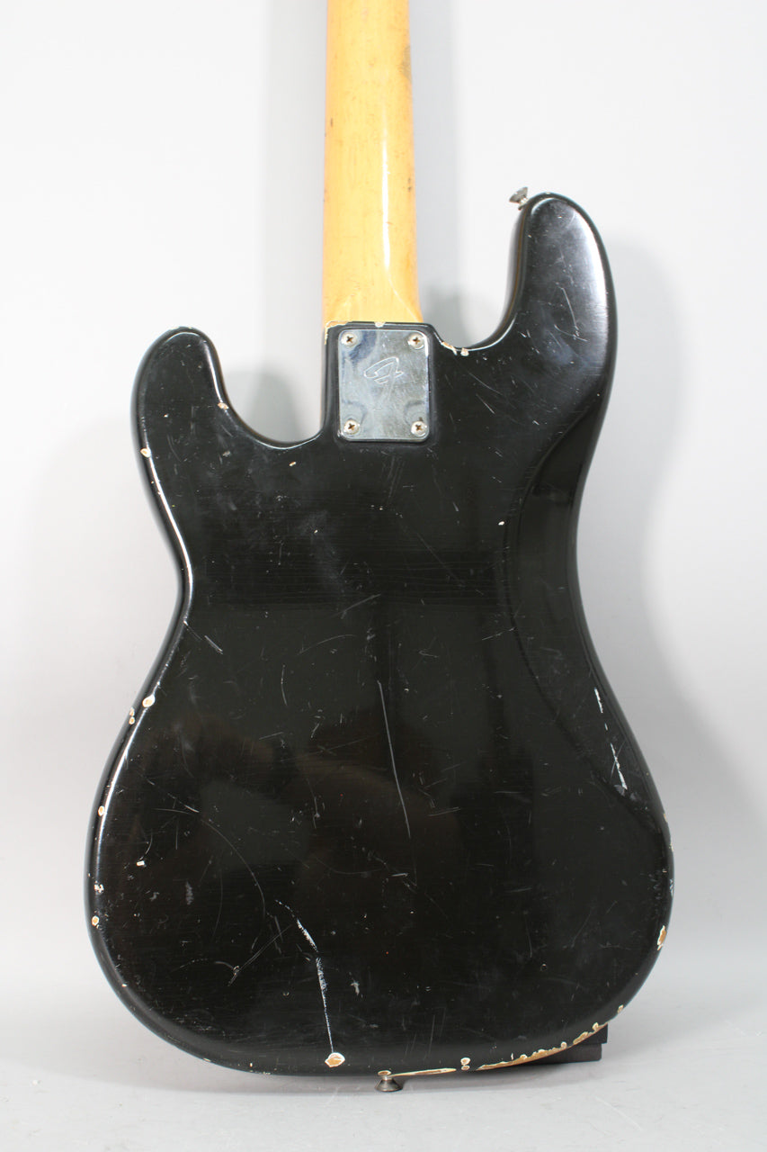 The back of a black bass guitar with a maple neck, showing heavy wear, scratches, and paint chips revealing wood underneath.