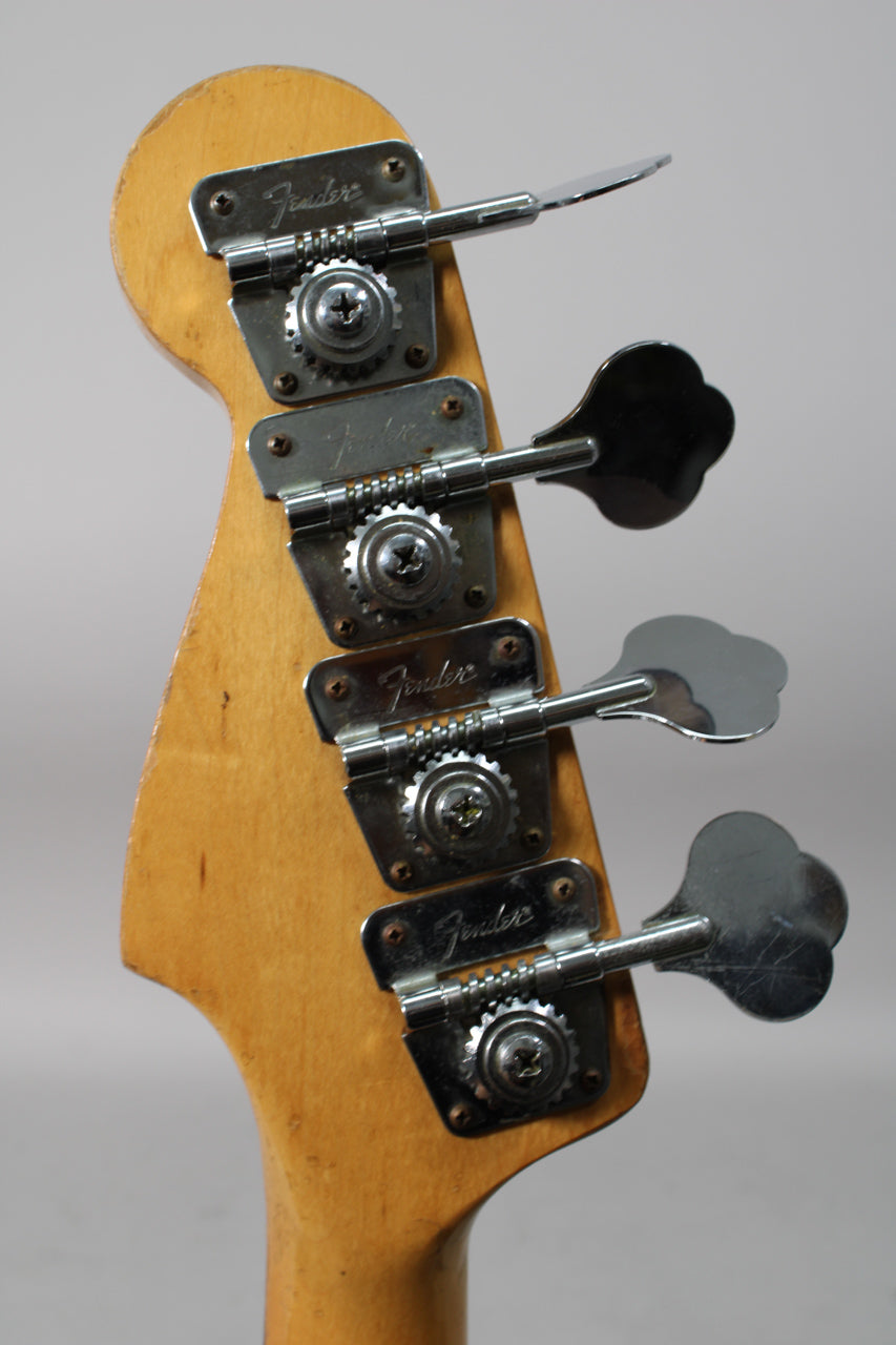 Close-up of the bass headstock from behind, showing four chrome clover-leaf tuners on a worn light wood finish.