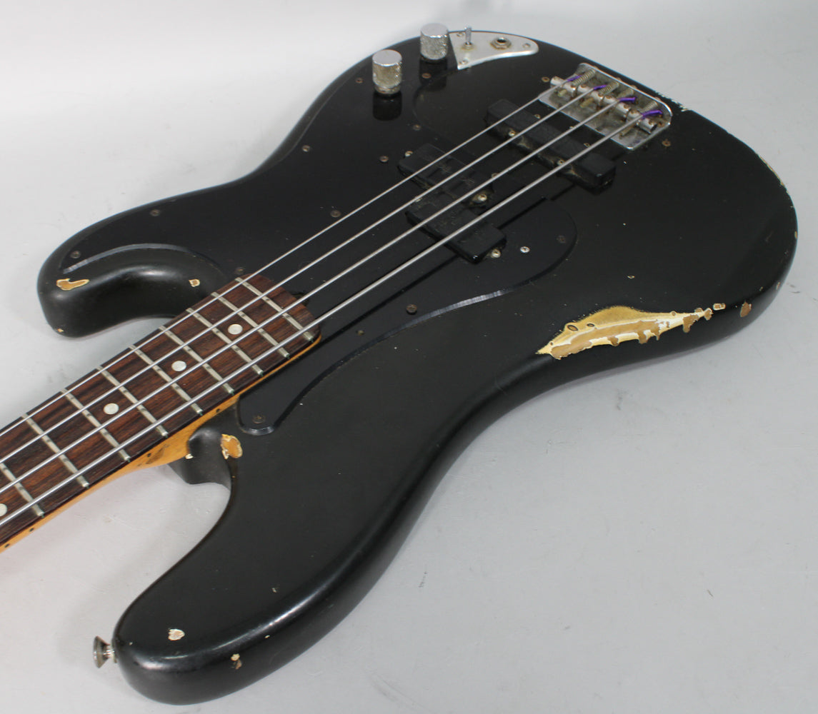 Black bass guitar, angled from the neck, showing extensive paint chipping on the lower bout and near the neck pocket.