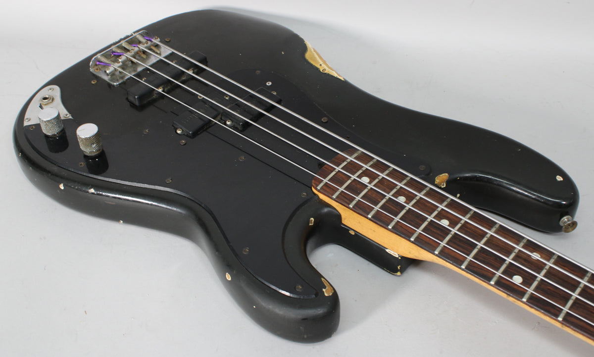Black bass guitar body and neck, angled from upper left, showing two knurled chrome knobs and significant paint wear.