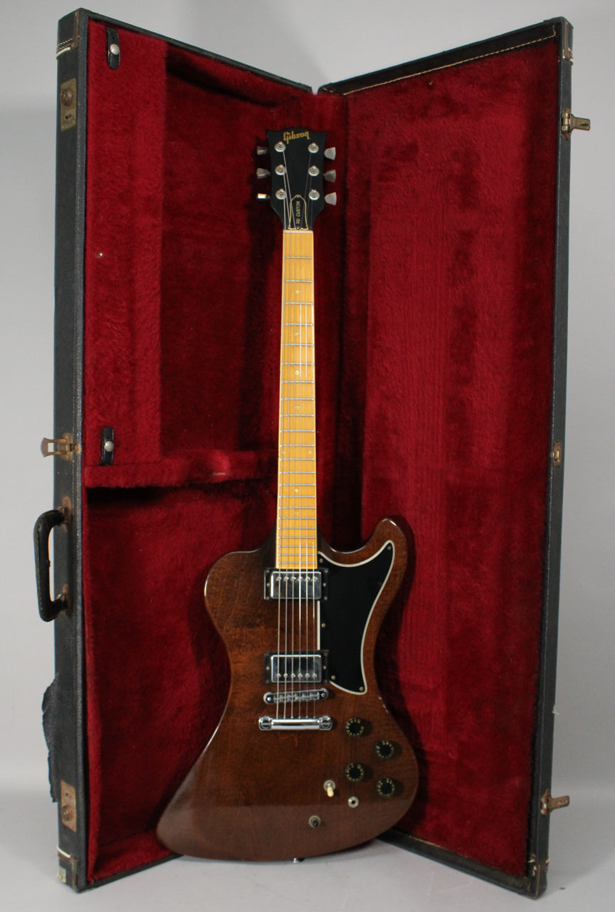 Full view of a dark walnut electric guitar with black pickguard and knobs, resting in a red velvet-lined open hard case.