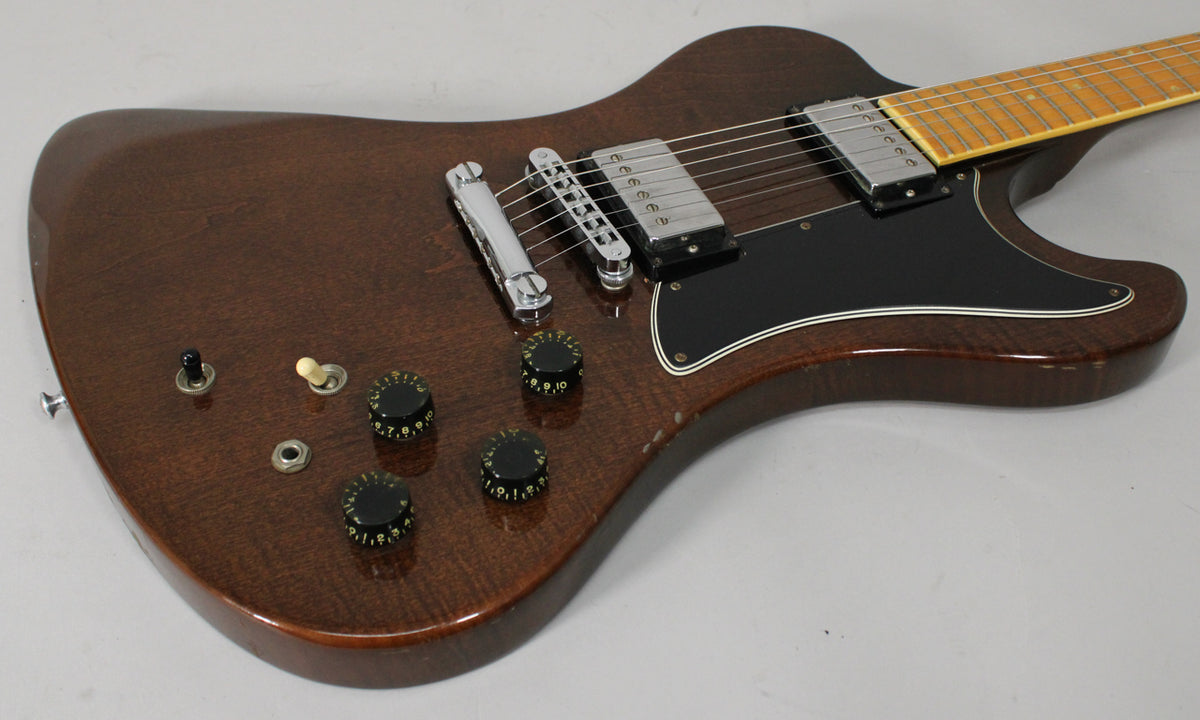 The walnut-finished electric guitar body, with visible wood grain, shows four black numbered control knobs and a black pickguard.