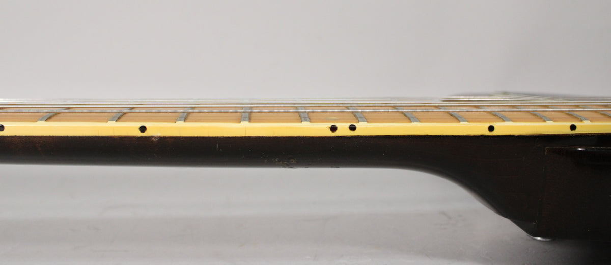 The guitar's dark walnut neck and body join, showing the cream binding, frets, and side dot markers, with some wear on the neck.