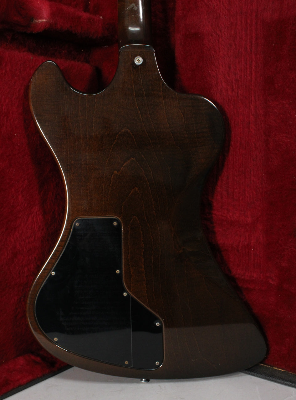 The back of a dark walnut guitar body with visible wood grain, two black control cavity covers, and a neck joint screw.