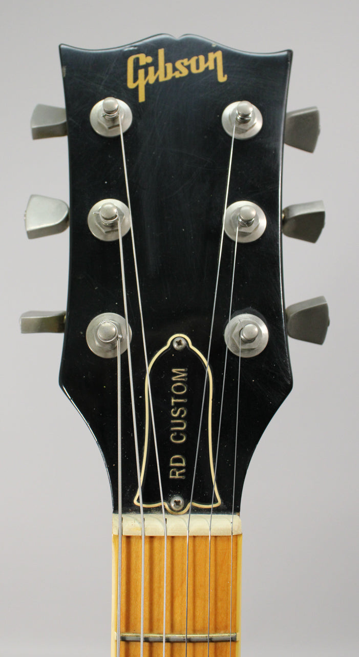Close-up of the black headstock with a gold logo, showing six silver tuners, light wear, and the top of the fretboard.