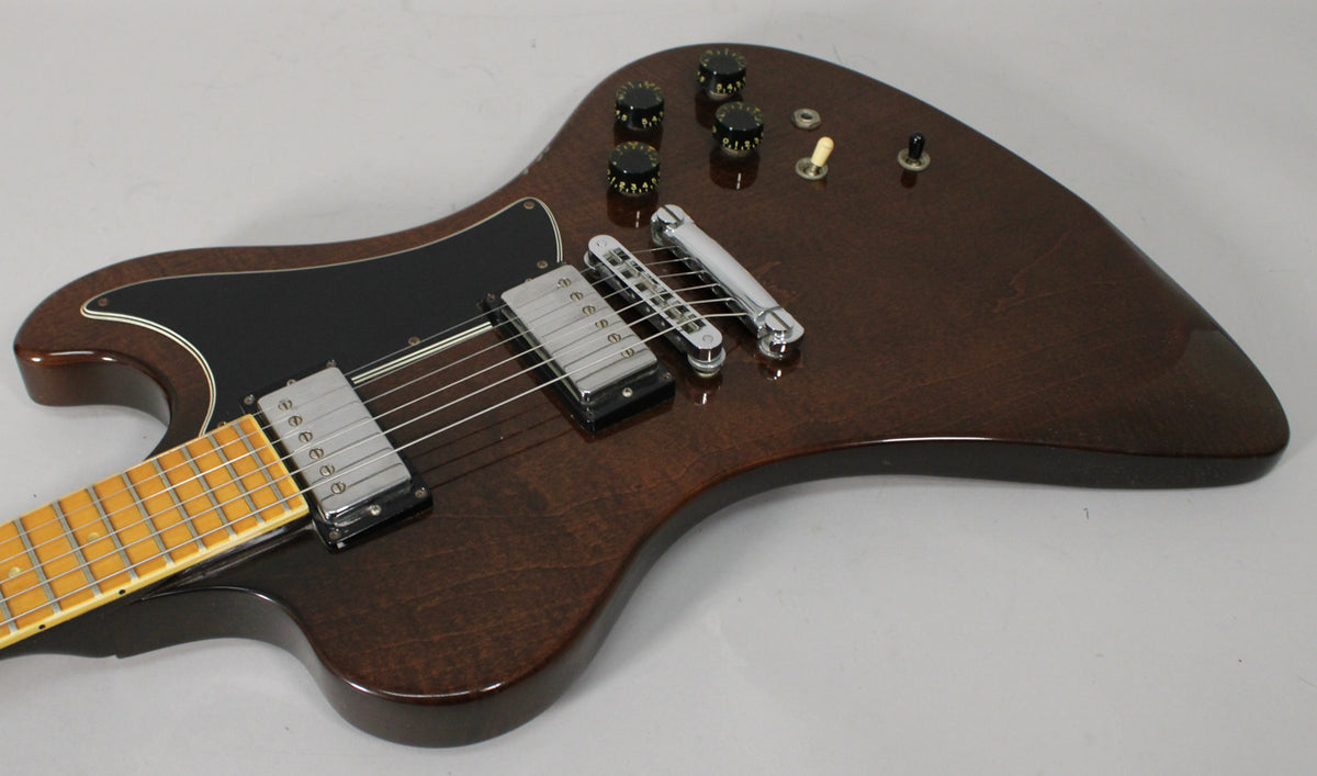 The upper body of a dark walnut electric guitar with a black pickguard, two chrome humbuckers, and four black control knobs.