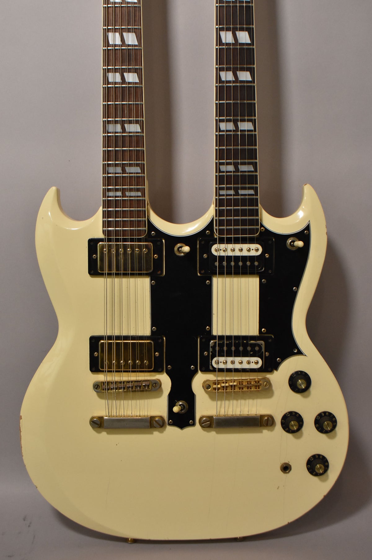 Full-frame view of the cream double-neck guitar, showing both necks, black pickguard, gold hardware, and four control knobs.