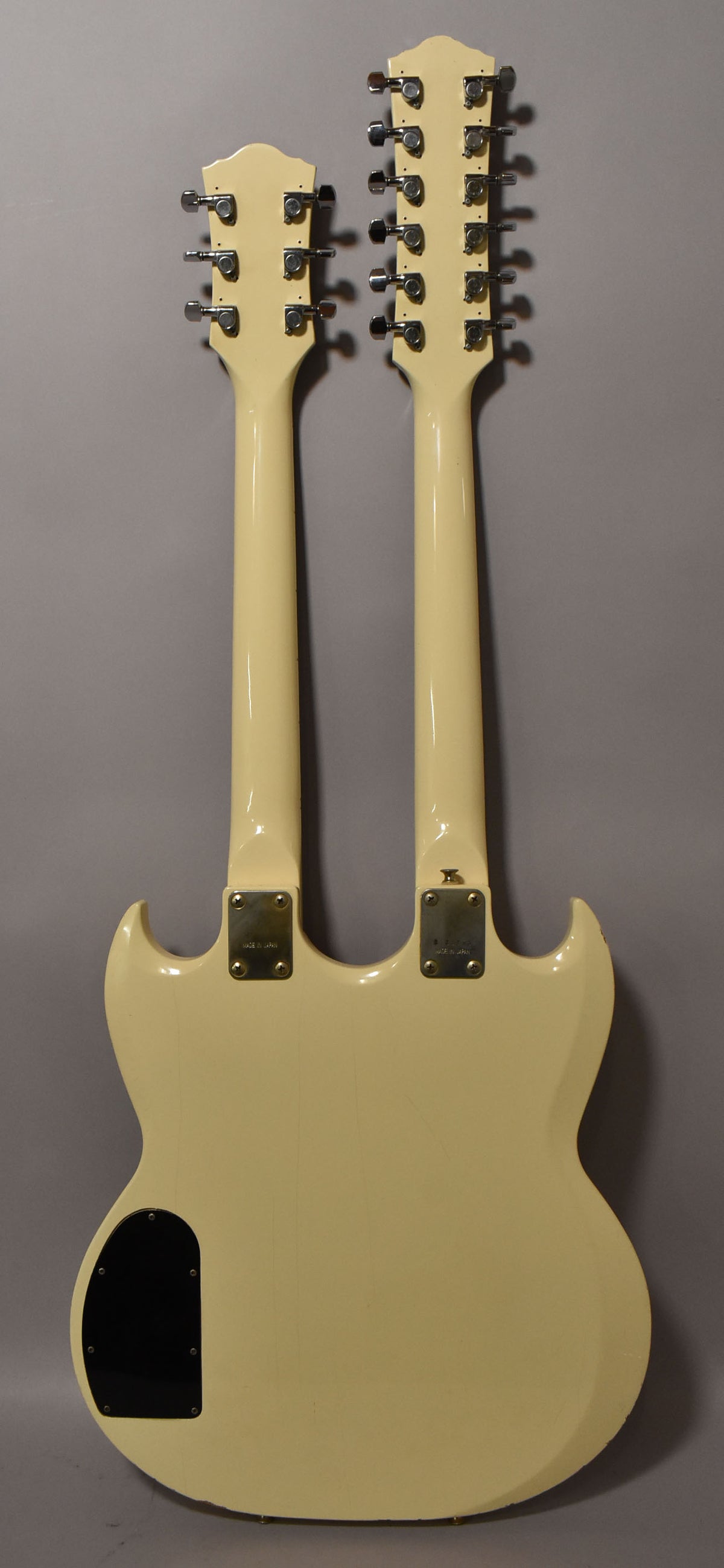 The back of a cream double-neck guitar, showing a 6-string and 12-string neck, with a black control cavity cover.